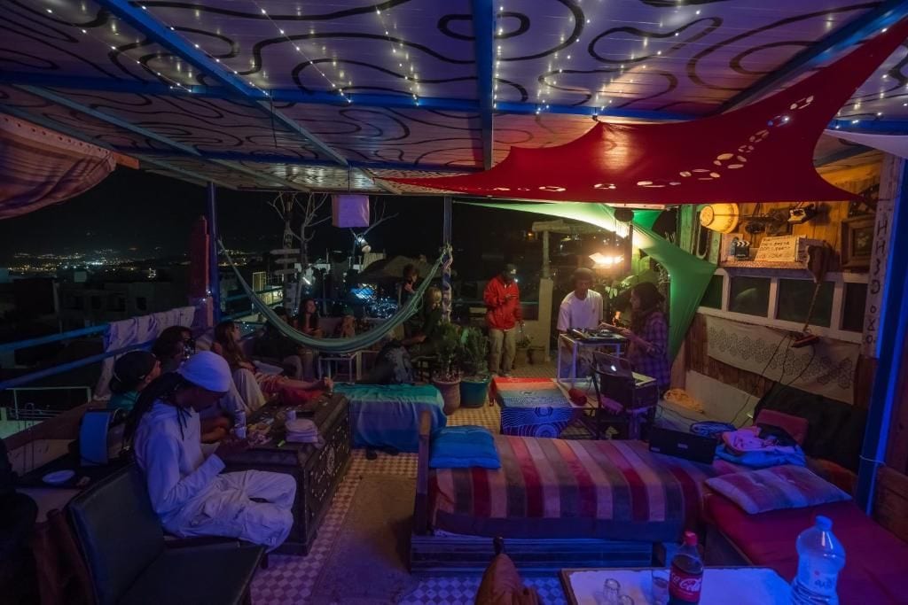 A rooftop terrace with seating areas, a hammock, and a view of the city at night.