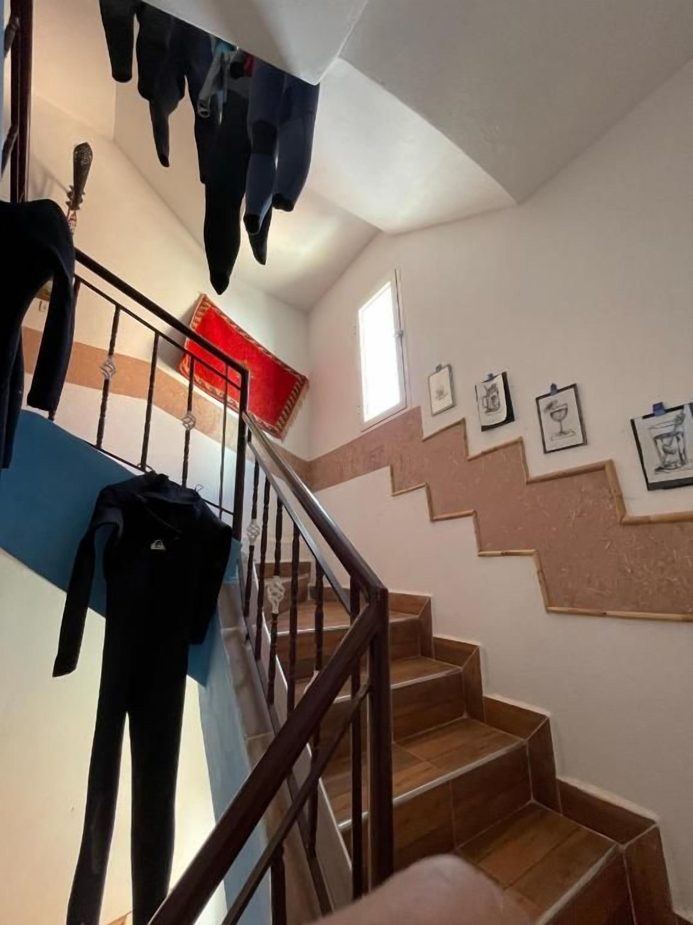 Una escalera con peldaños de madera y barandilla de metal, que conduce a un rellano con alfombra roja.