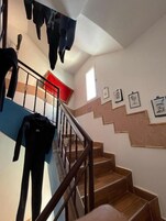 Una escalera con peldaños de madera y barandilla de metal, que conduce a un rellano con alfombra roja.