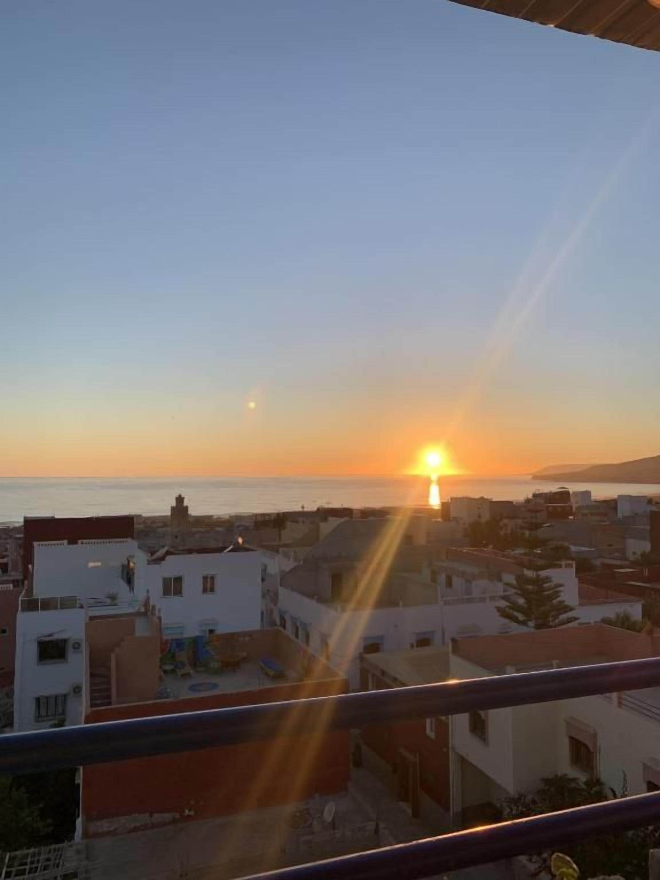 A sunset view from a balcony overlooking a residential area with buildings and a clear sky.
