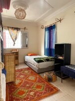 Un dormitorio con cama, armario, escritorio, silla, alfombra y ventana con cortinas.