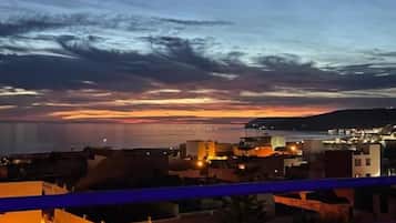 Varanda com vista para a paisagem urbana ao entardecer, com edifícios e um pôr do sol.