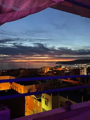 A balcony with a view of a cityscape at dusk, featuring buildings and a sunset. - Agachill Surf House (Aourir)