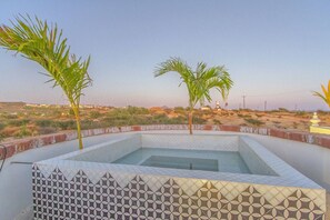Une piscine rectangulaire bordée d’un motif décoratif, entourée d’un petit muret, avec des palmiers et un paysage lointain.