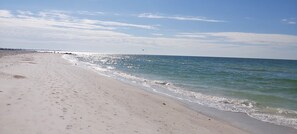 Ein weiter Sandstrand mit sanften Wellen, wolkenlosem Himmel und einer entfernten Küstenlinie.