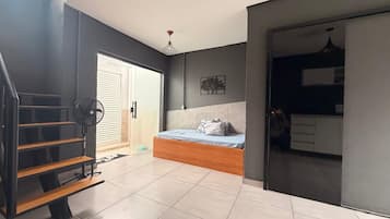 Quarto com cama, ventilador, escada e vista para uma cozinha.