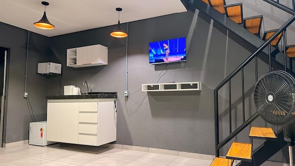 A modern kitchen with a built-in microwave, a white cabinet, and a TV mounted on the wall.