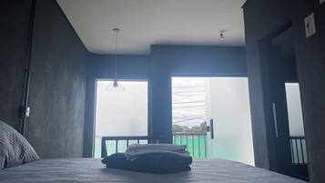 Ein Schlafzimmer mit Bett, einer Pendelleuchte, einem Fenster und Blick ins Freie.