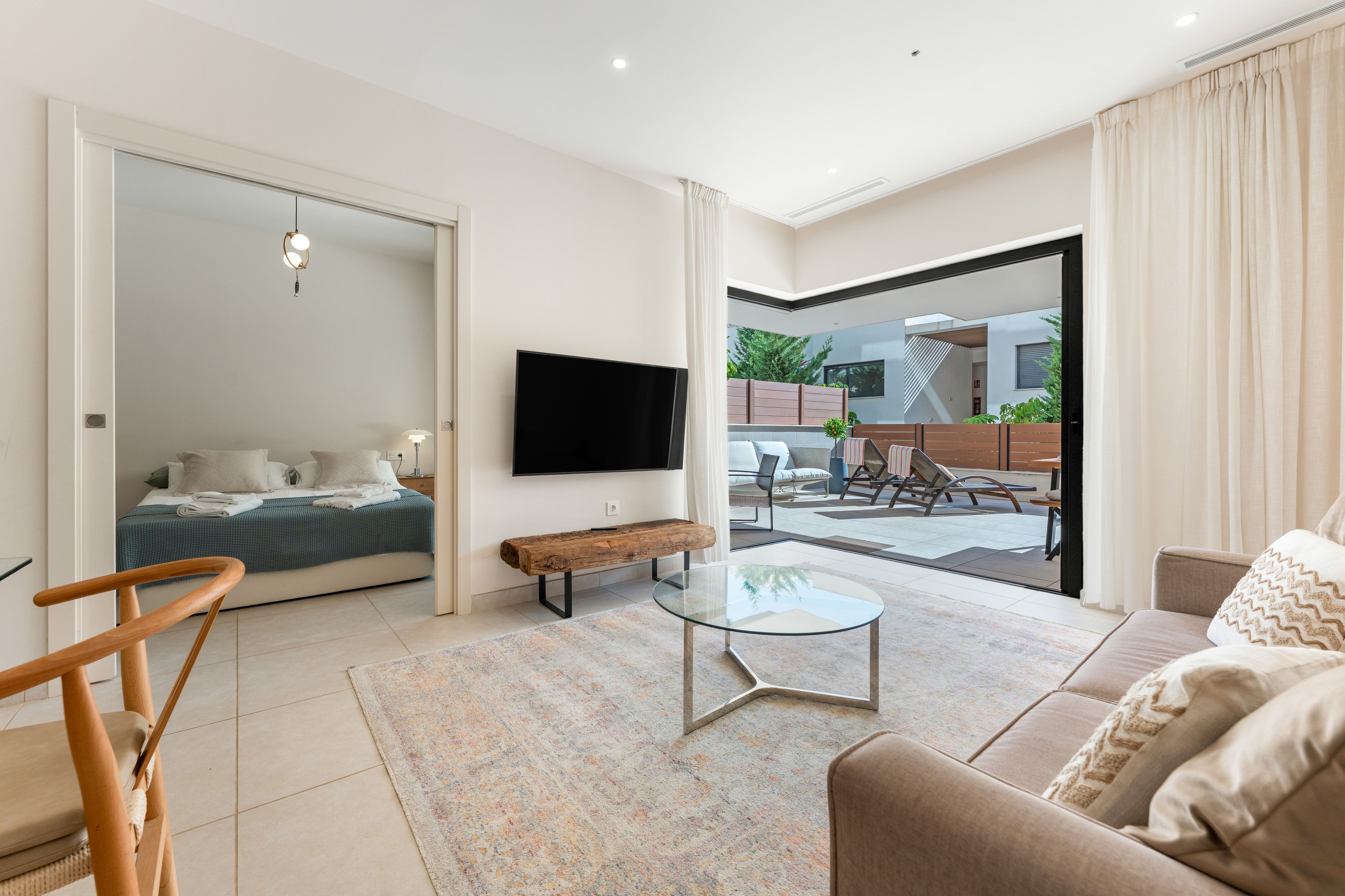 A modern living room with a sofa, a glass coffee table, and a TV mounted on the wall.