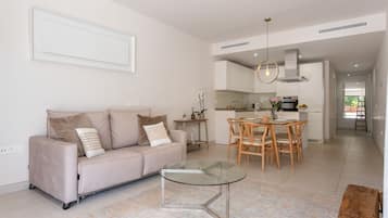 Ein modernes Wohnzimmer mit einem Glastisch, einem beigefarbenen Sofa und einem Essbereich mit Holzsesseln und einem Glastisch.