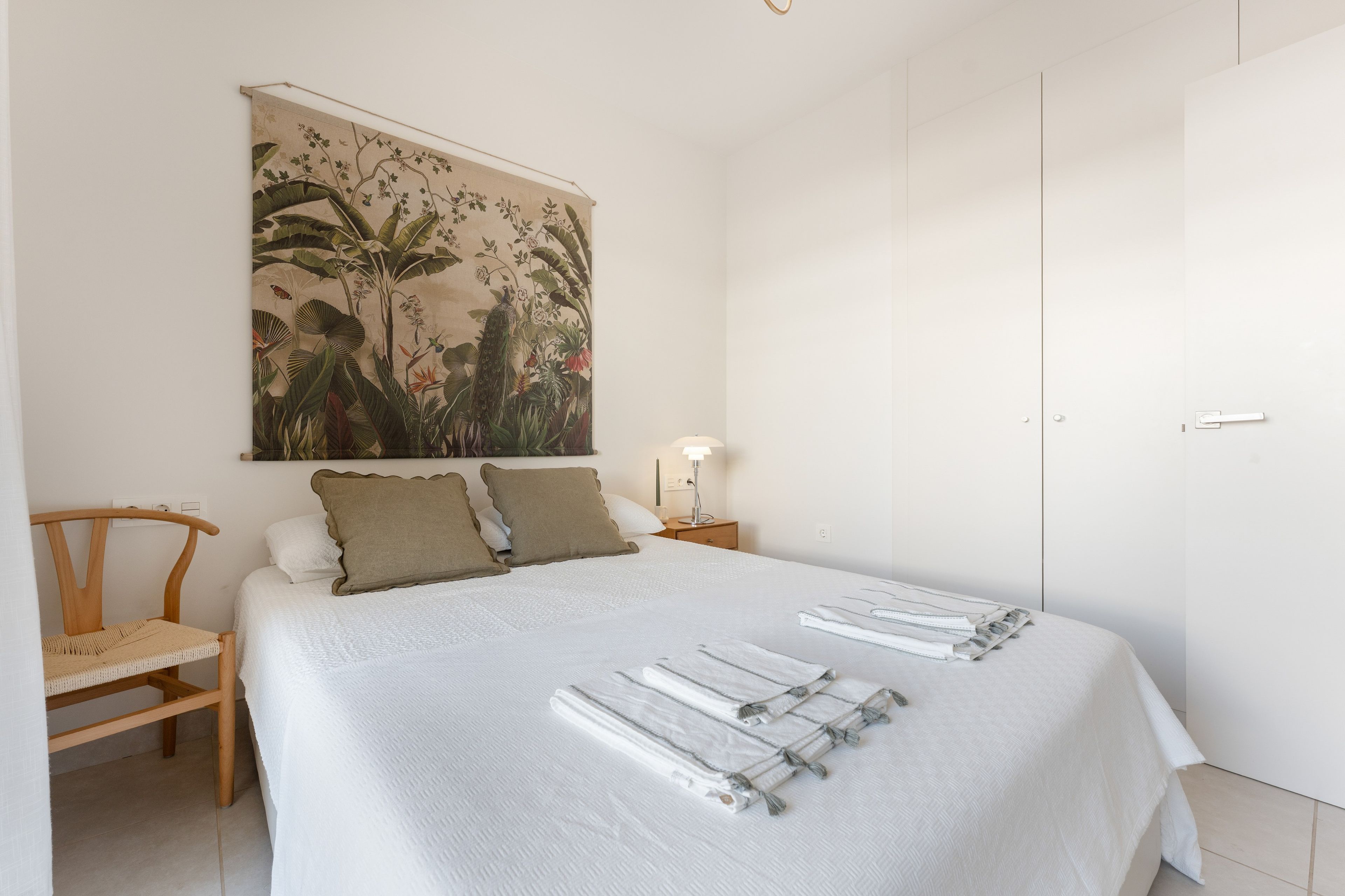 A bedroom with a bed, a chair, a nightstand with a lamp, and a door.