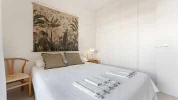 A bedroom with a bed, a chair, a nightstand with a lamp, and a door.