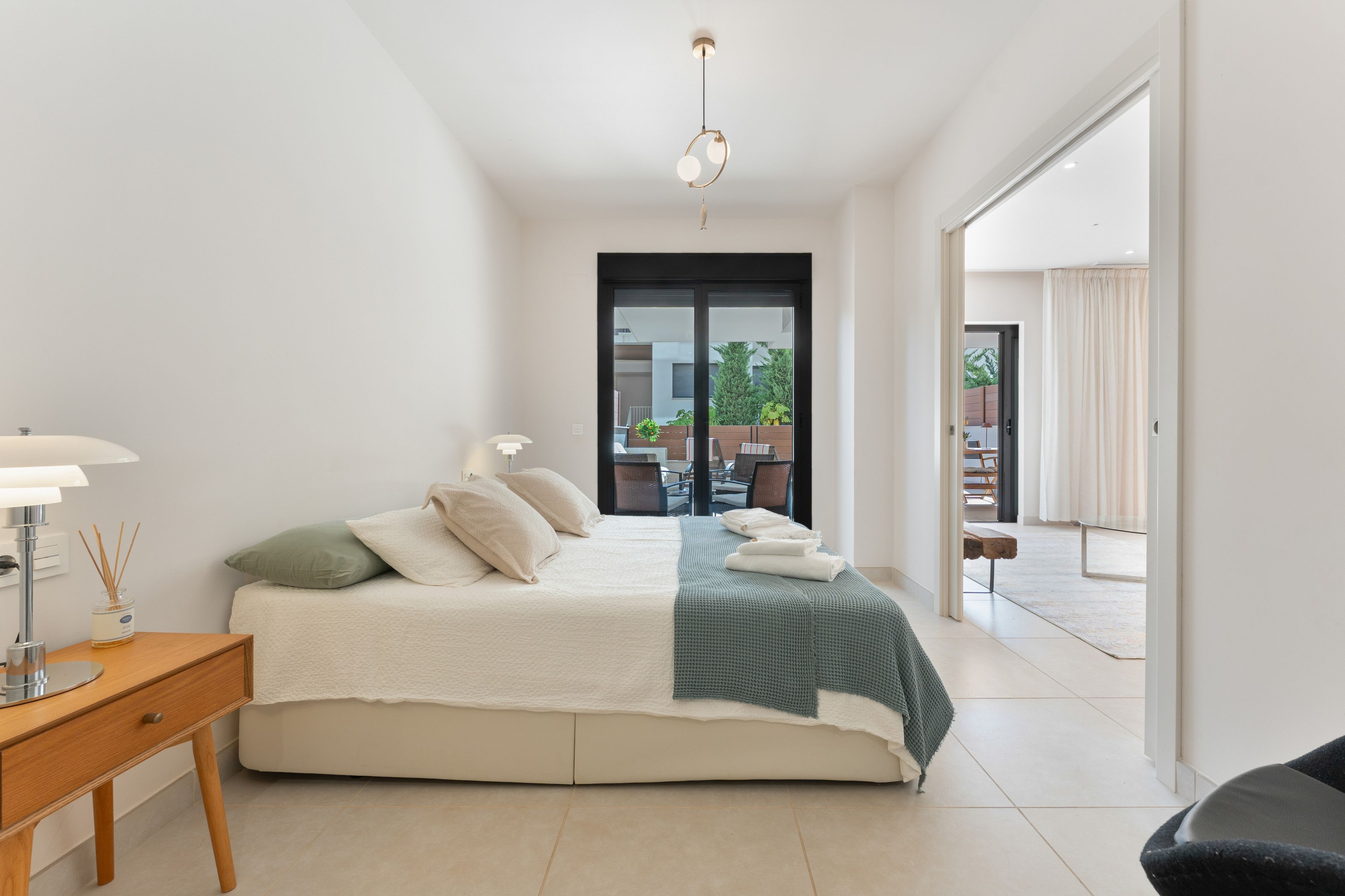 A modern bedroom with a bed, bedside table, lamp, and a view of the outdoors.