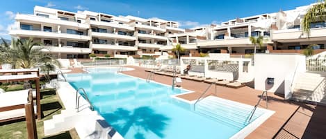 Un hotel moderno con piscina, varios balcones y un césped bien cuidado.