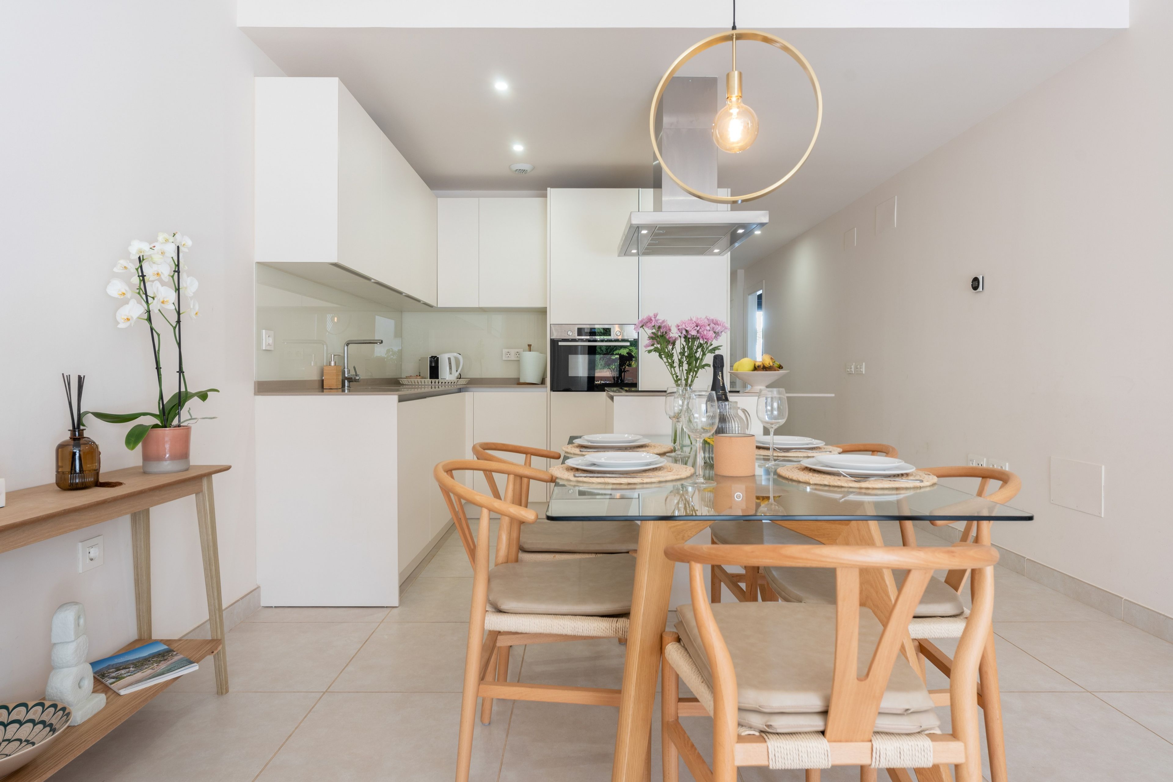 Una cocina moderna con armarios blancos, una isla central y un comedor con mesa de vidrio y sillas de madera.