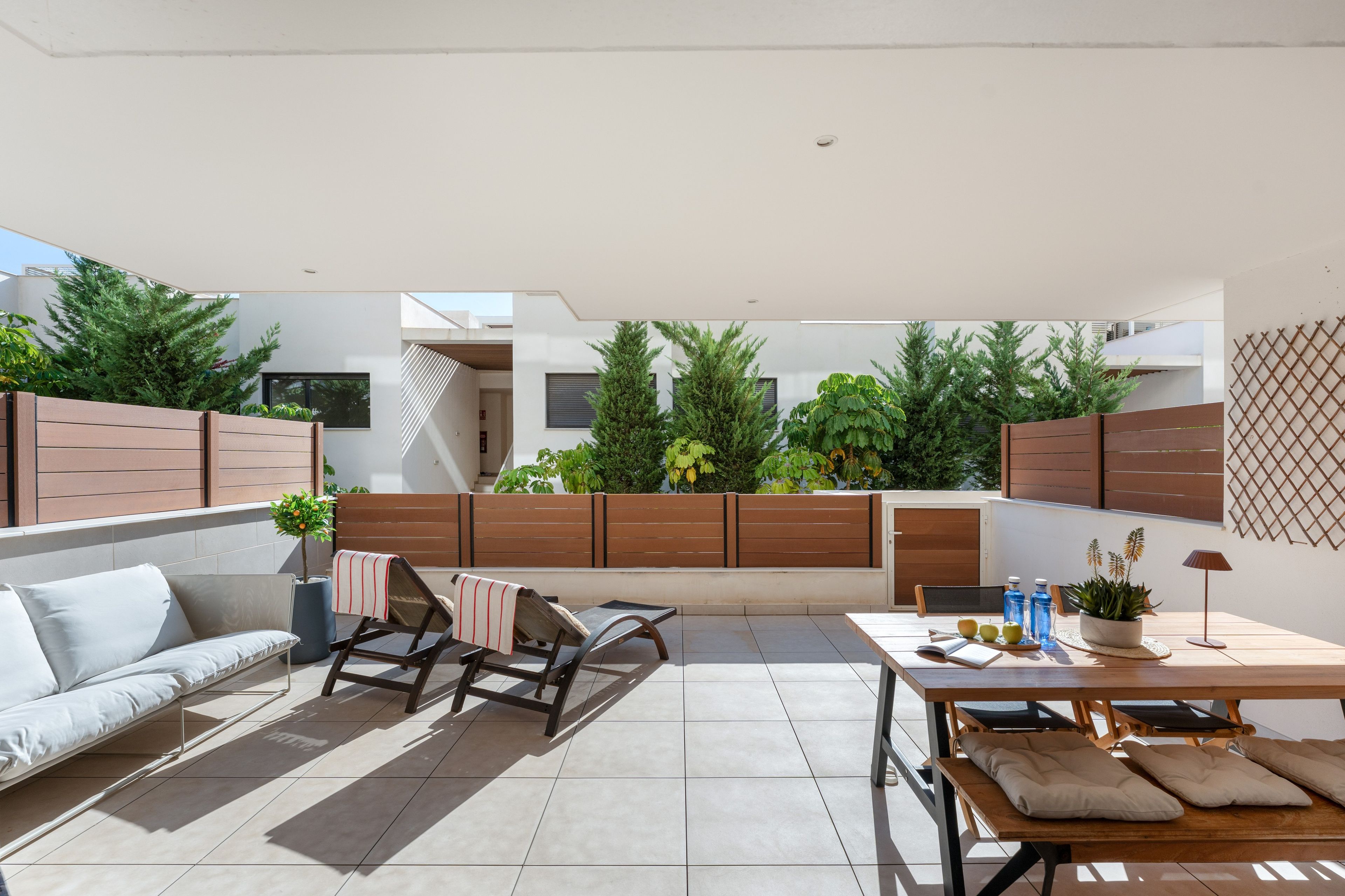 A modern outdoor living space with a sofa, lounge chairs, a dining table, and potted plants.