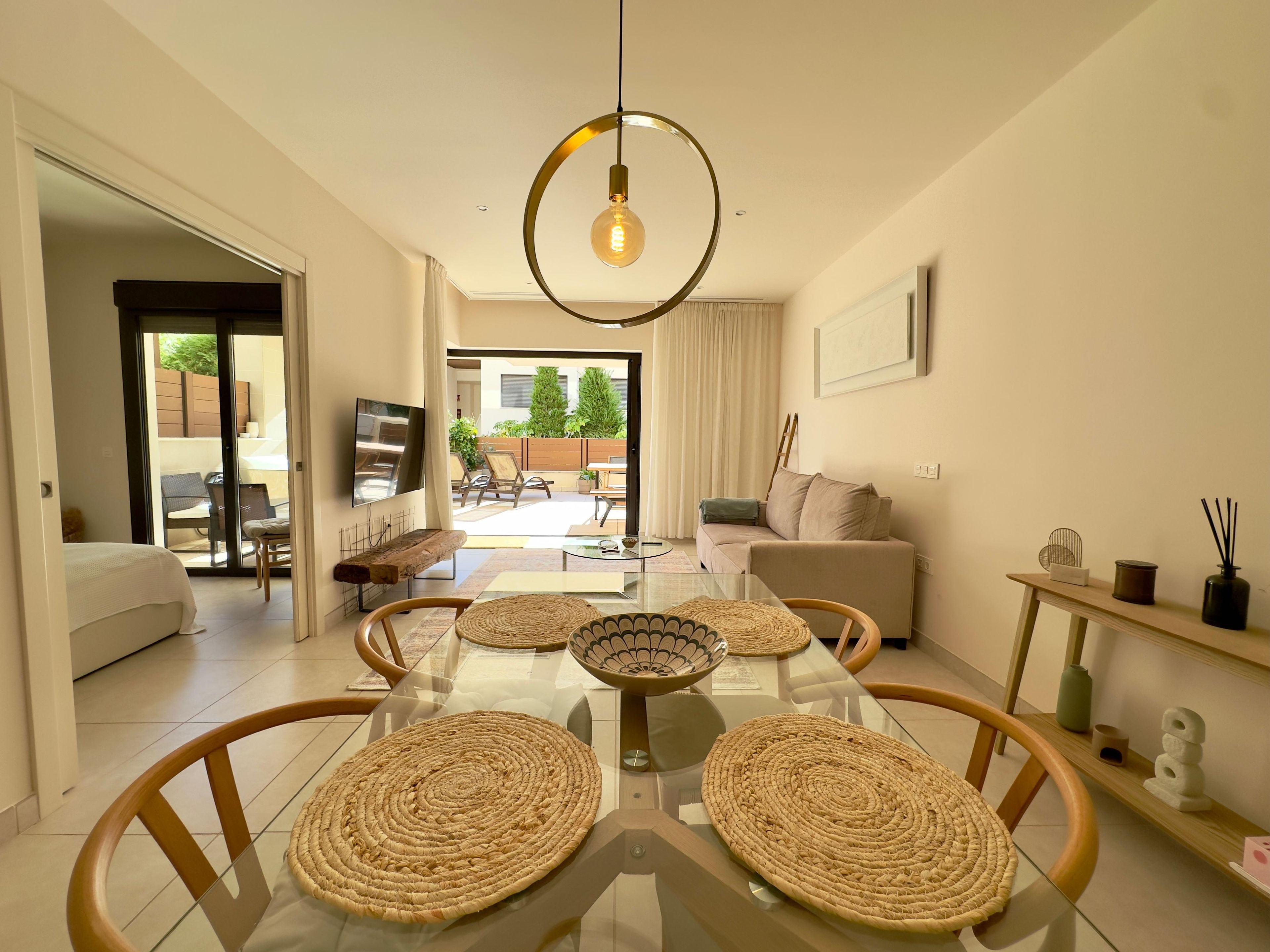 A modern living room with a glass dining table, woven placemats, a sofa, and a television.