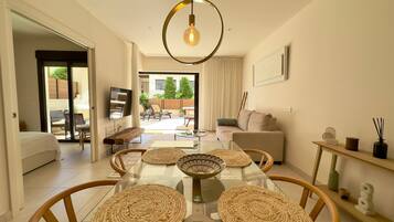A modern living room with a glass dining table, woven placemats, a sofa, and a television.
