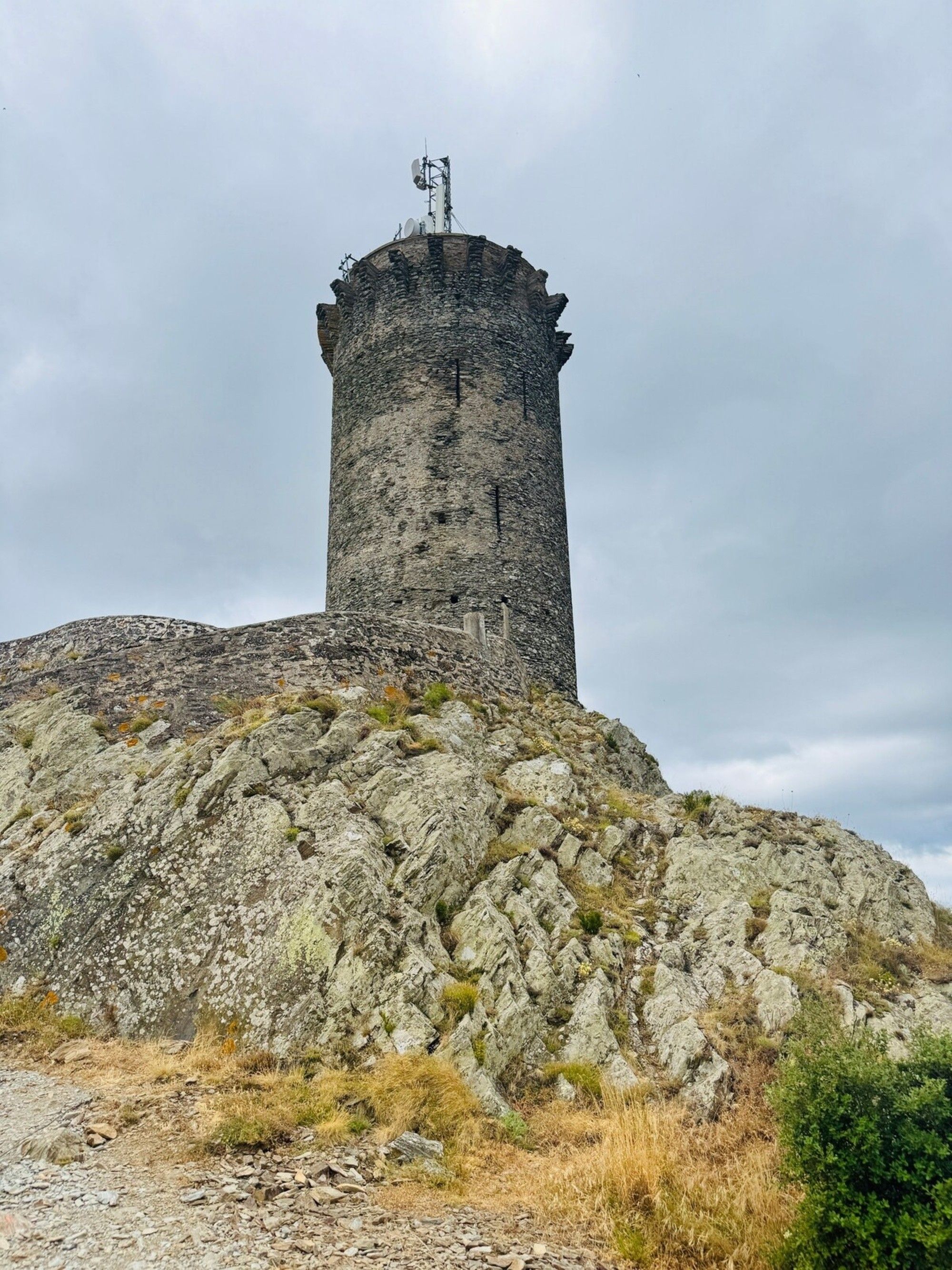 A stone tower with a weather vane on top, situated on a rocky hill.