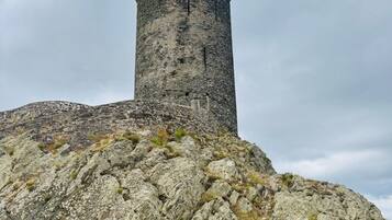A stone tower with a weather vane on top, situated on a rocky hill.