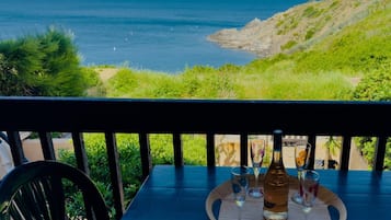 Ein Tisch mit einer Flasche und Gläsern, mit Blick auf eine Küstenlandschaft mit Meer und Hügeln.