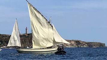 En segelbåt med ett stort segel på vattnet, en klippig kustlinje och en fyr i bakgrunden.