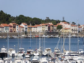 Un puerto deportivo con barcos amarrados, un paseo marítimo con edificios de colores y un paisaje montañoso de fondo.