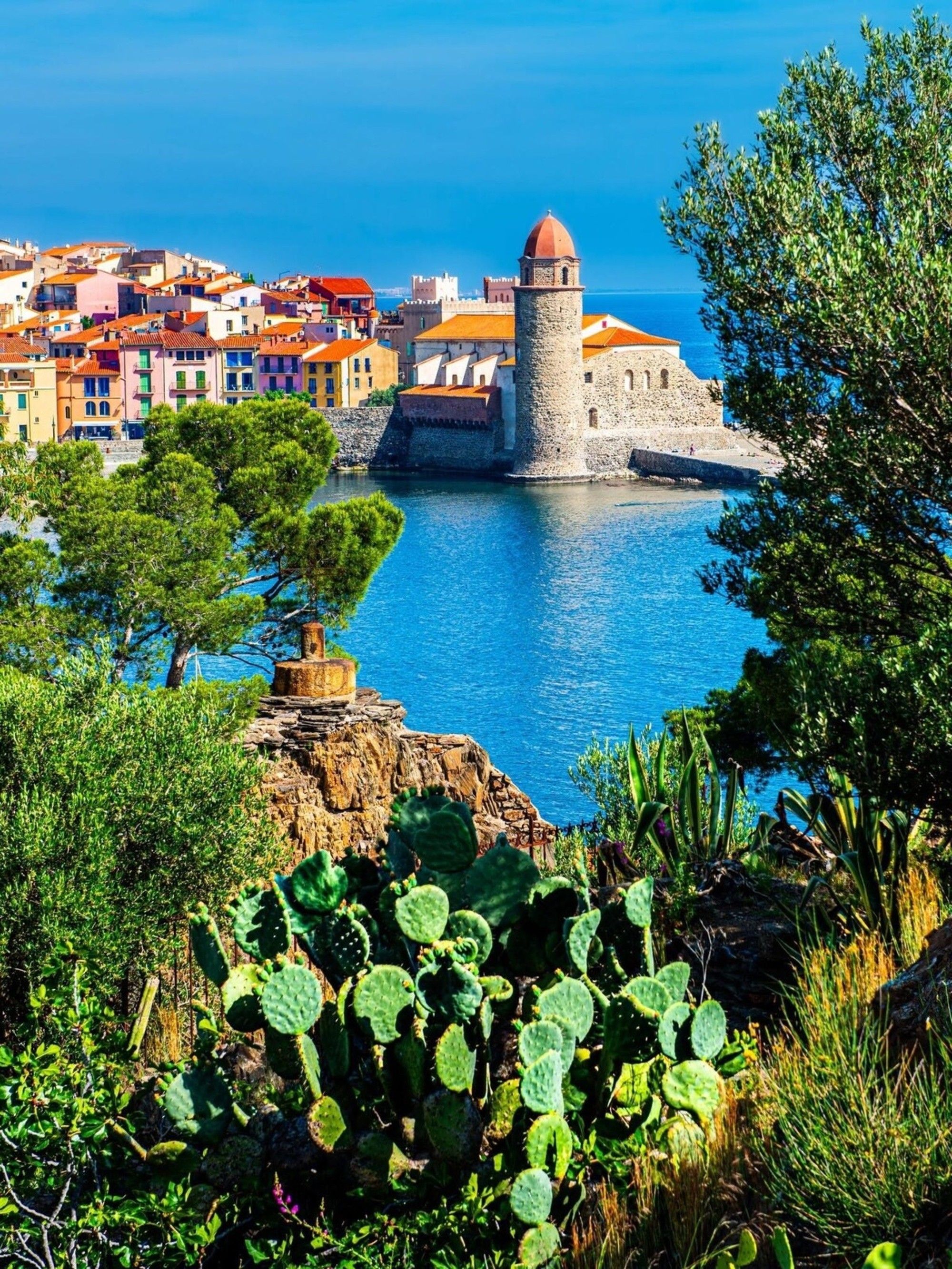 A coastal town with colorful buildings, a prominent tower, and a clear view of the sea.