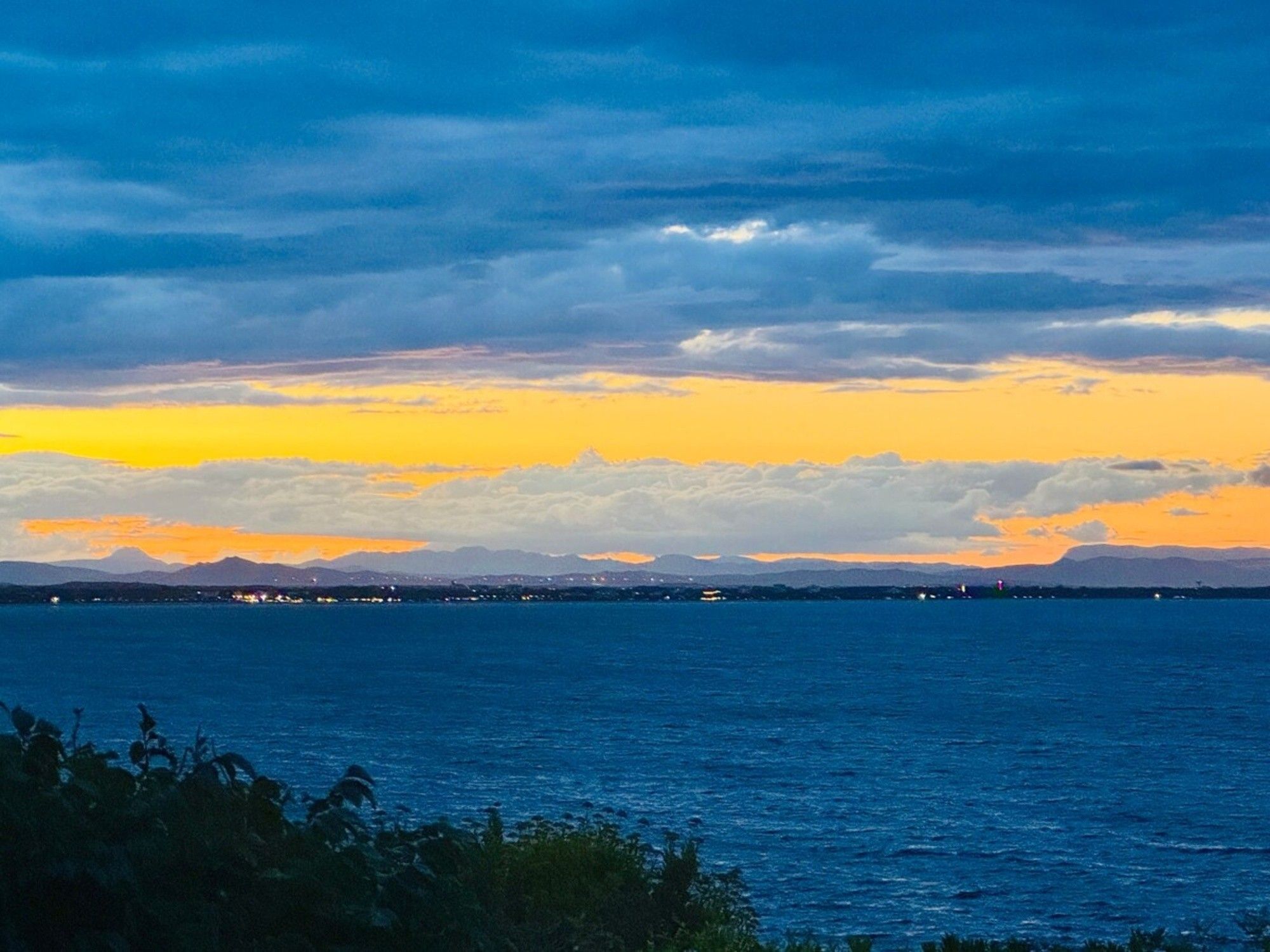 A coastal landscape with a view of the sea and distant mountains under a twilight sky.