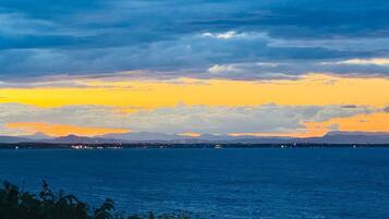 A coastal landscape with a view of the sea and distant mountains under a twilight sky.