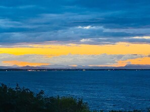 Un paysage côtier offrant une vue sur la mer et les montagnes lointaines, sous un ciel crépusculaire.