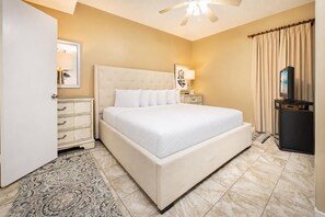 A bedroom with a large bed, bedside tables, a ceiling fan, a TV, and a patterned rug. - Phoenix East 1202 1 Bedroom Condo (Orange Beach)