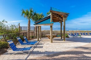 Un espace de détente aménagé sur la plage, avec des chaises longues bleues, une pergola en bois et des palmiers.