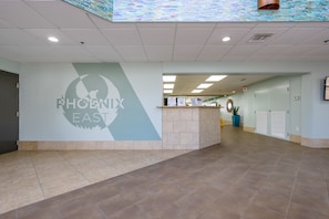 Un hall d’entrée spacieux avec un comptoir de réception, un logo fixé au mur et un sol carrelé.