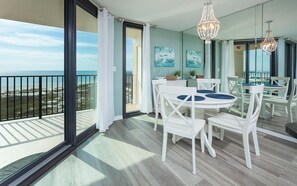 A balcony with a view of the beach, a dining area with white furniture, and a chandelier. - Phoenix East 308 1 Bedroom Condo (Orange Beach)