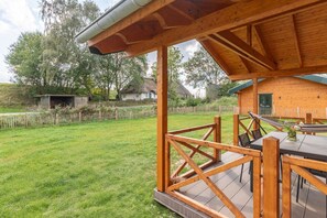 Eine Holzterrasse mit Tisch und Stühlen, umgeben von einem eingezäunten Garten mit Rasen und Bäumen.