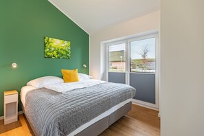 Ein Schlafzimmer mit einem Bett, einem Nachttisch, einer grünen Wand, einem Fenster und Blick nach draußen.