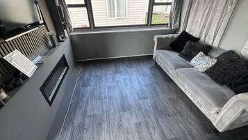 Una sala de estar moderna con un sofá gris, una chimenea y un ventanal con cortinas.