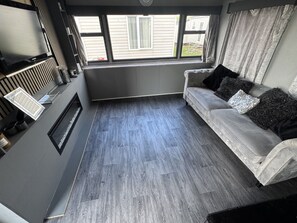 Un salon moderne avec un canapé gris, une cheminée et une grande fenêtre avec des rideaux.