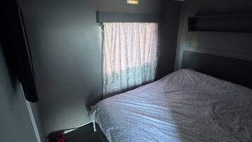 Una habitación pequeña con una cama, un ventanal con cortinas, una lámpara de techo y un televisor de pared.