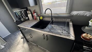 A compact kitchen with a black sink, a window with blinds, and a dish rack.