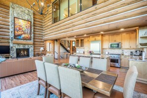 A spacious living area with a fireplace, a dining table, and a kitchen with wooden cabinets and modern appliances. - Pine And Peak 4 Bedroom Home (Telluride)