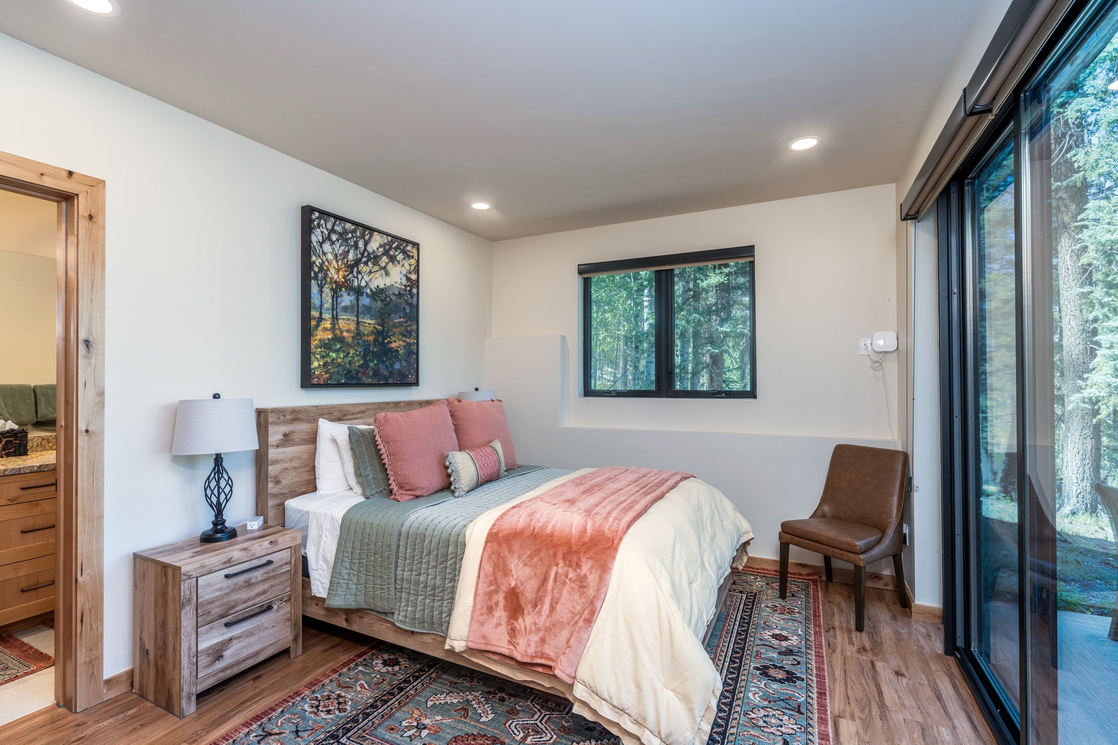 A bedroom with a bed, a nightstand, a chair, a window, and a painting on the wall.