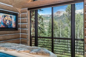 A log cabin room with a large window, a painting of a bear, and a fur-covered bed. - Pine And Peak 4 Bedroom Home (Telluride)