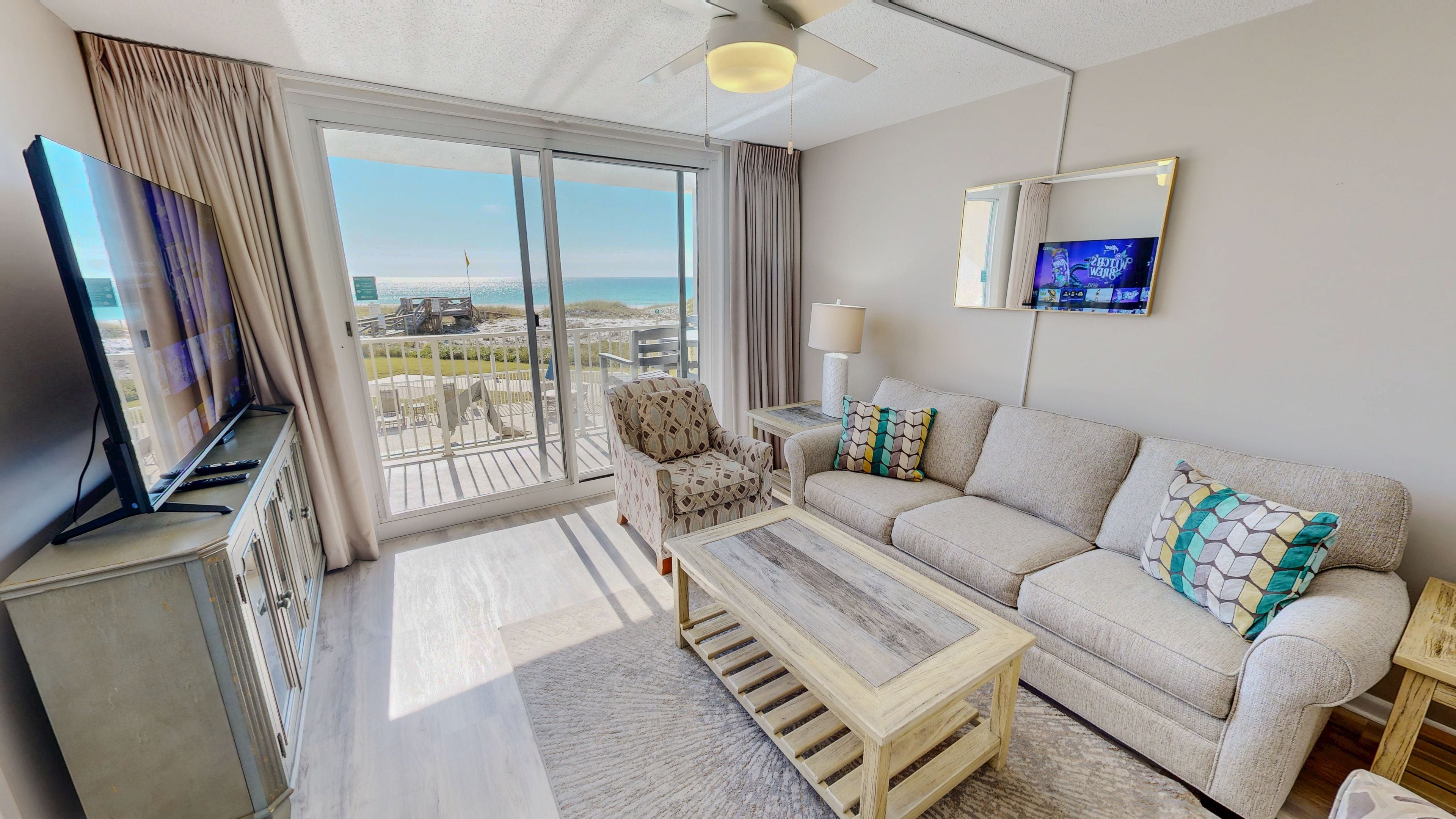 Una sala de estar moderna con un sofá, un sillón, una mesa de centro, un televisor y un balcón con vista al mar.