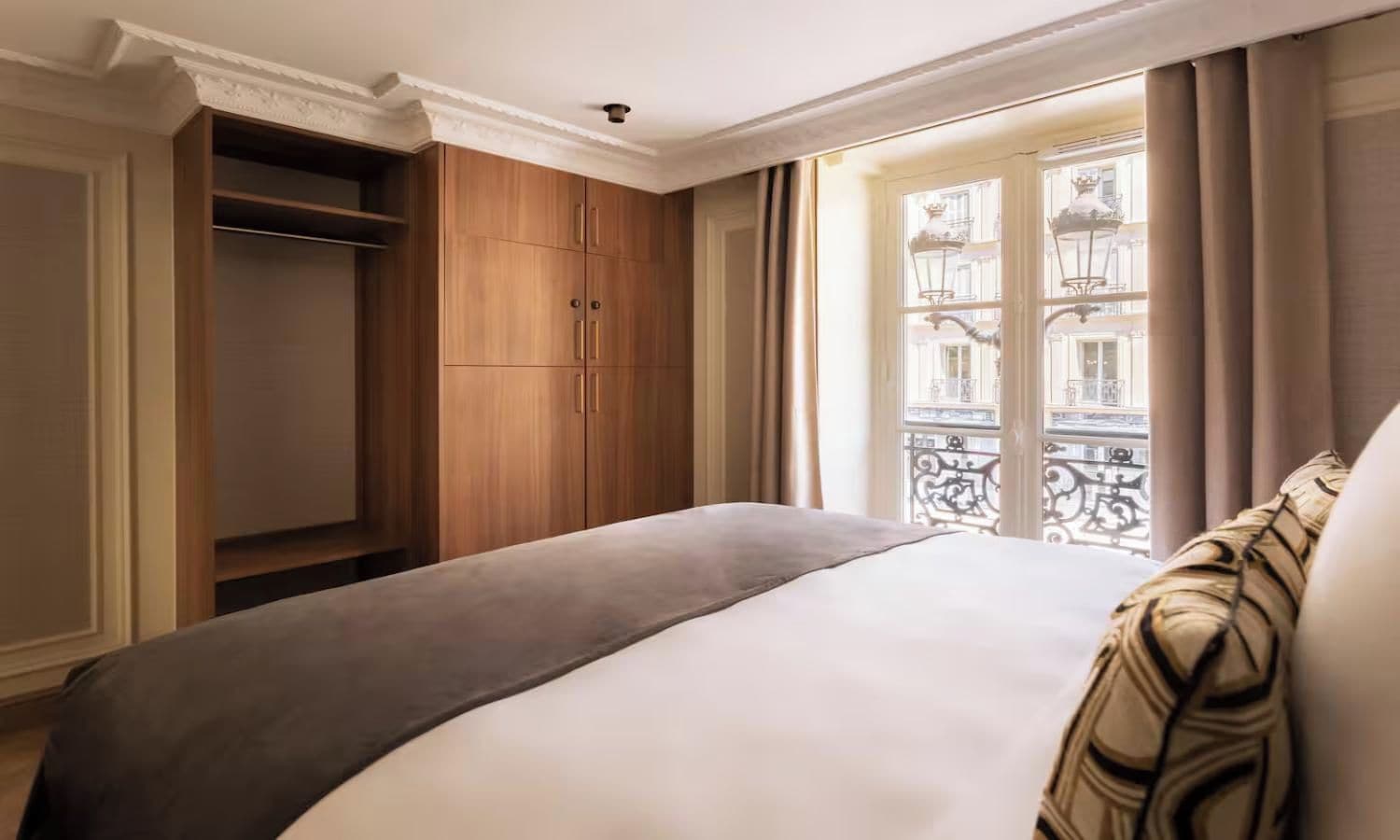 A hotel room with a bed, a wardrobe, and a window with a view of buildings.