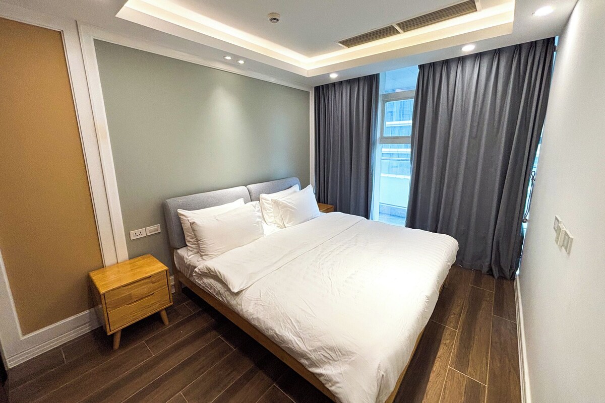 A modern bedroom with a large bed, a nightstand, and a window with curtains.