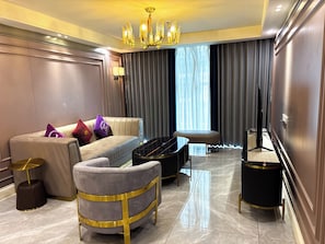 A modern living room with a sofa, armchair, and ottoman, a black piano, a television, and a chandelier. - Grand Marina Residences (Paranaque)