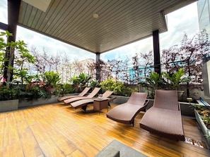 A covered outdoor area with wooden flooring, lounge chairs, and potted plants. - Grand Marina Residences (Paranaque)