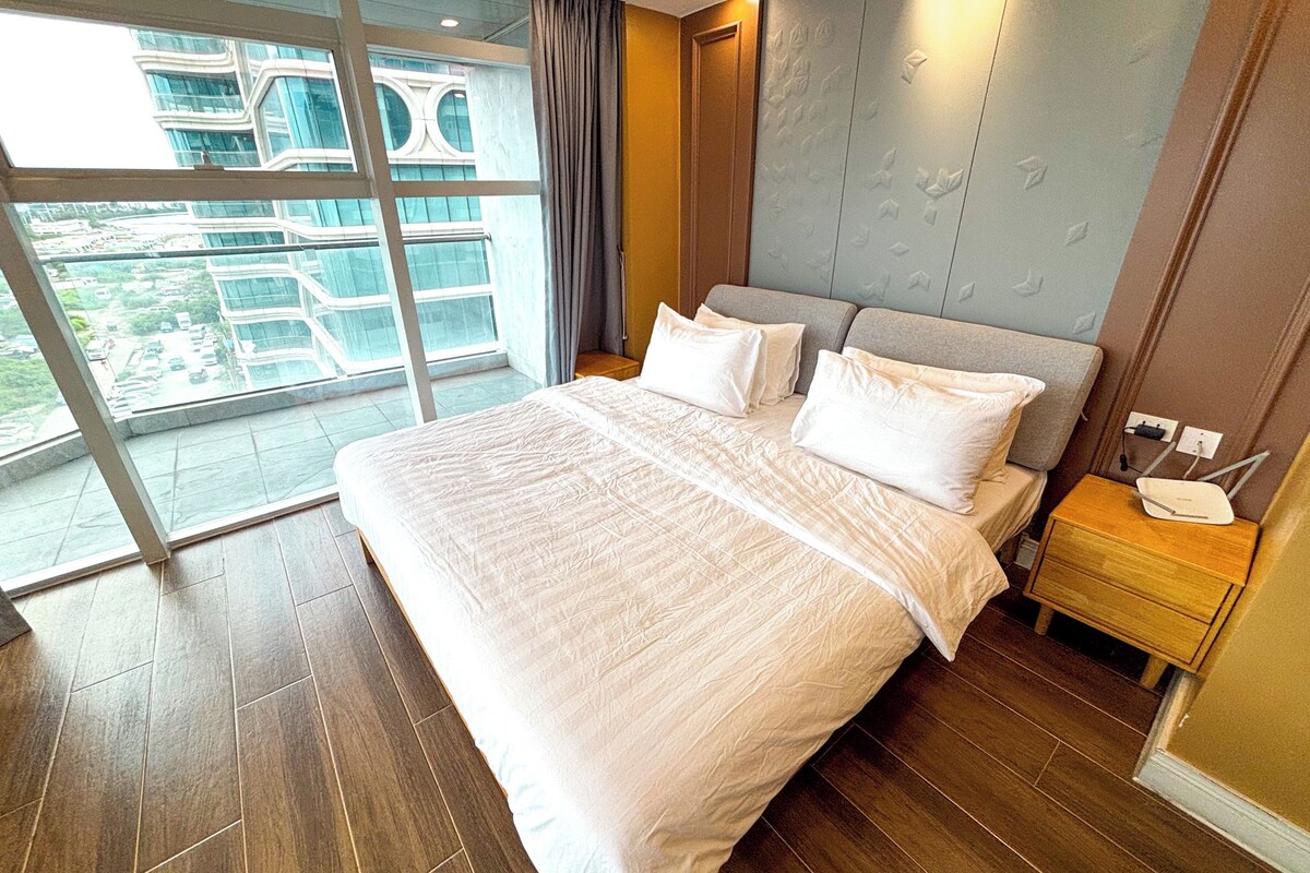 A modern hotel room with a large bed, a nightstand, and a view of a building through the window.